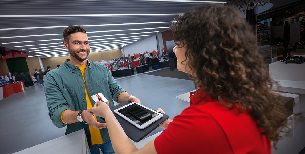 Ein Mann gibt einer Mitarbeiterin von MediaMarktSaturn ein Tablet und bekommt eine Gutscheinkarte zurück